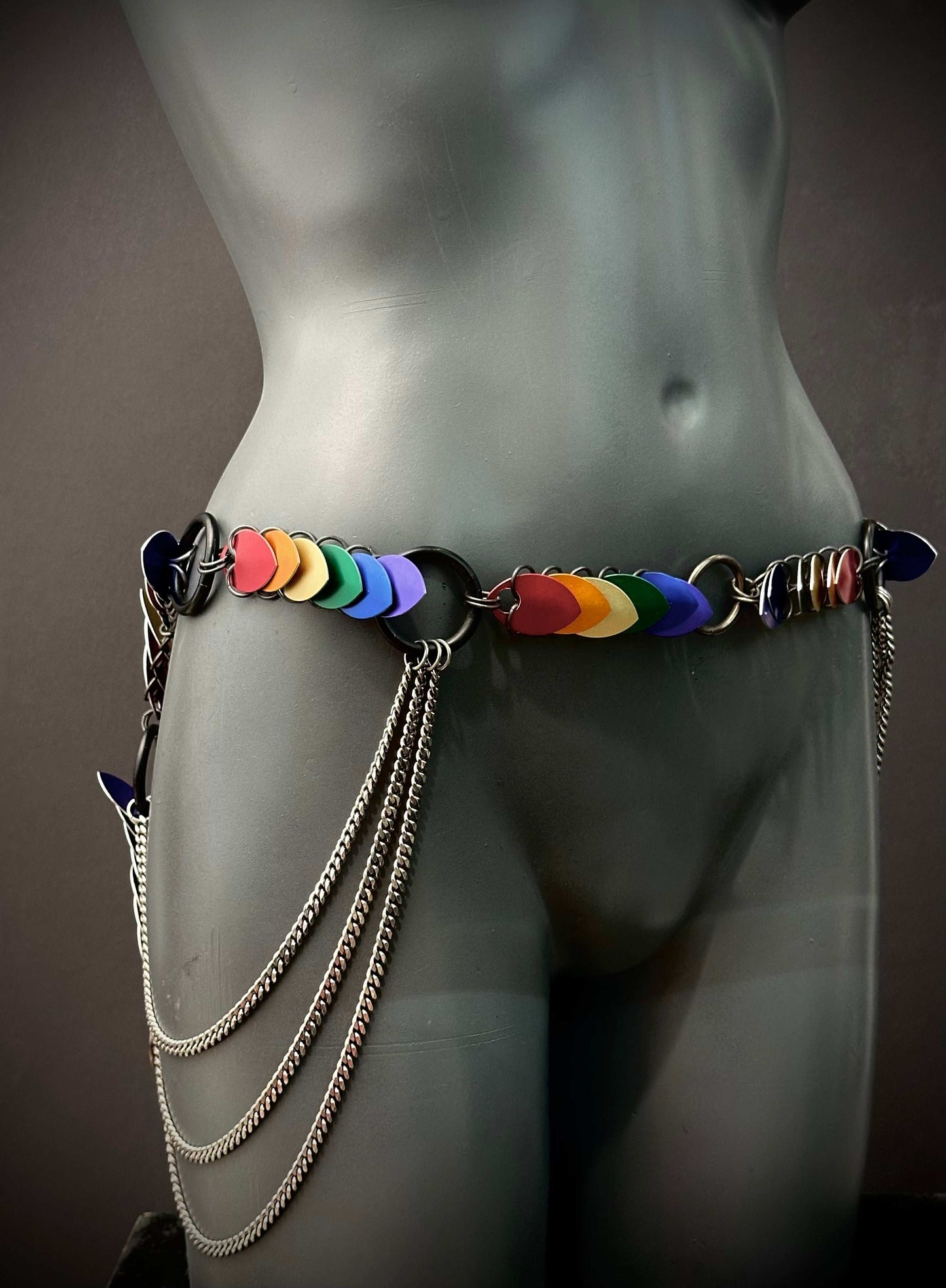 Colorful heart-shaped belt with metal chains on gray mannequin, vibrant and edgy style, bold emotion