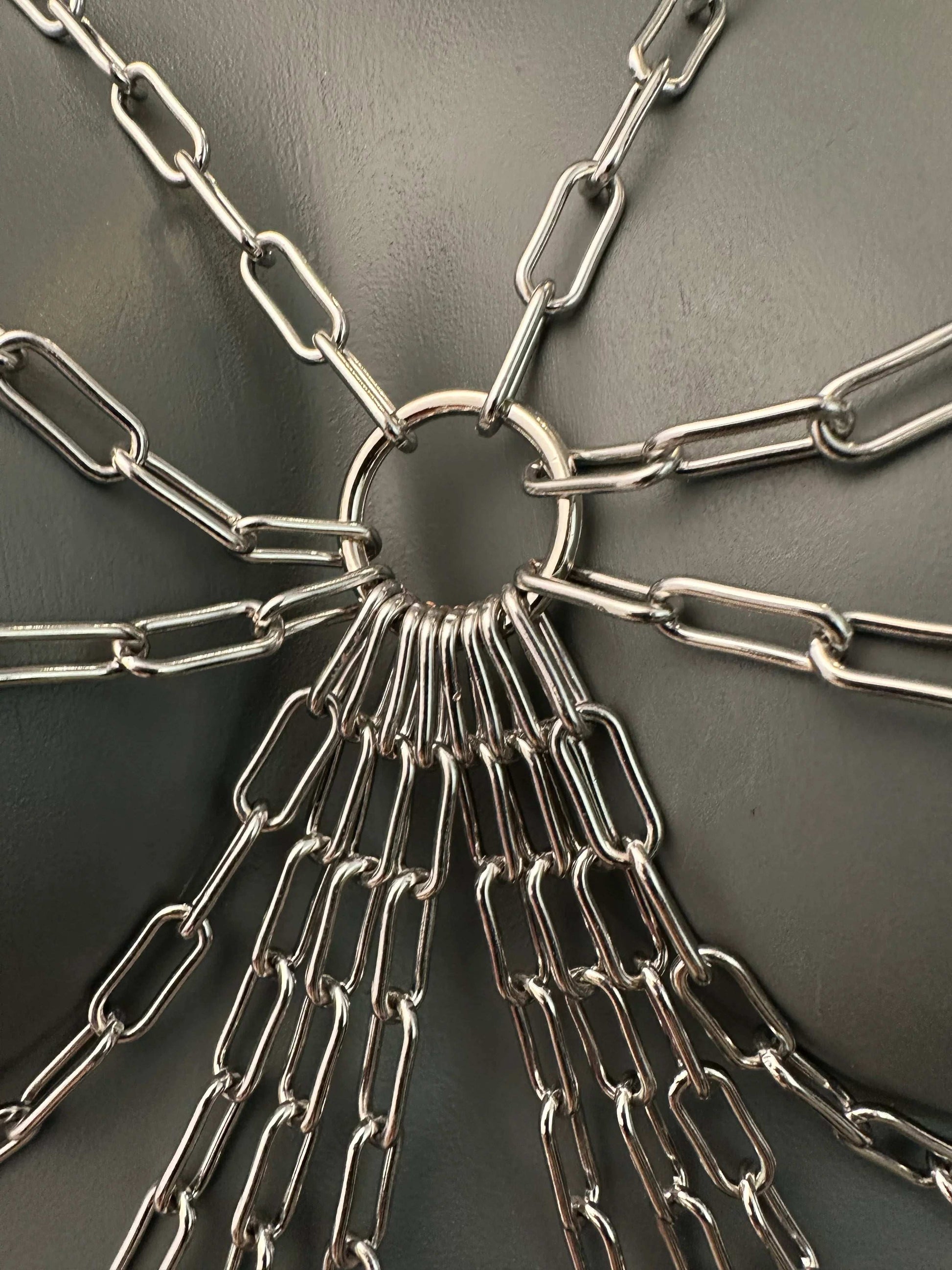 Silver metal chains connected to a central ring on gray surface, industrial and strong feeling