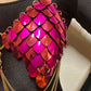 Metal scale bra in pink and red with gold chains on black fabric, bold and vibrant style