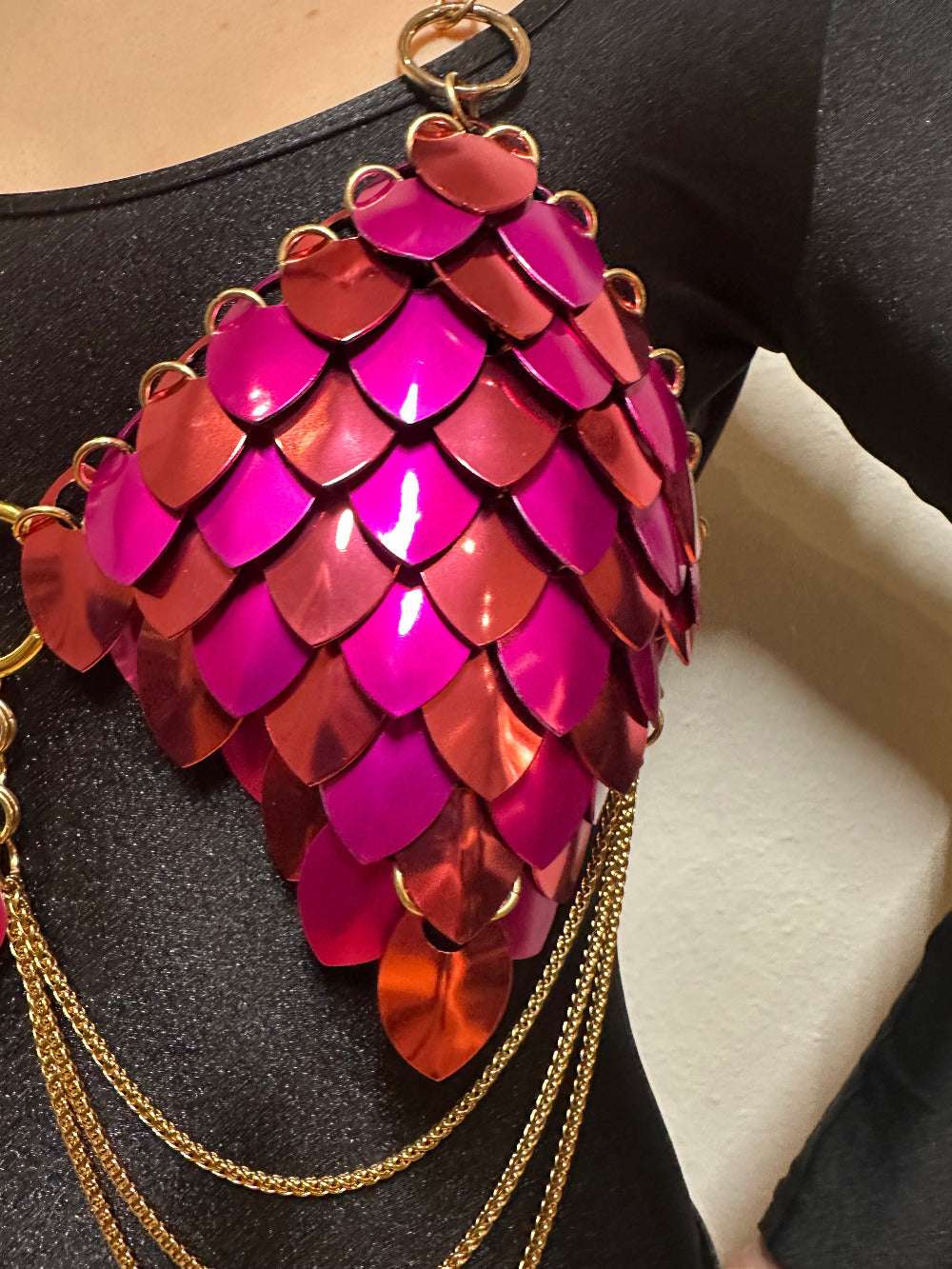 Metal scale bra in pink and red with gold chains on black fabric, bold and vibrant style
