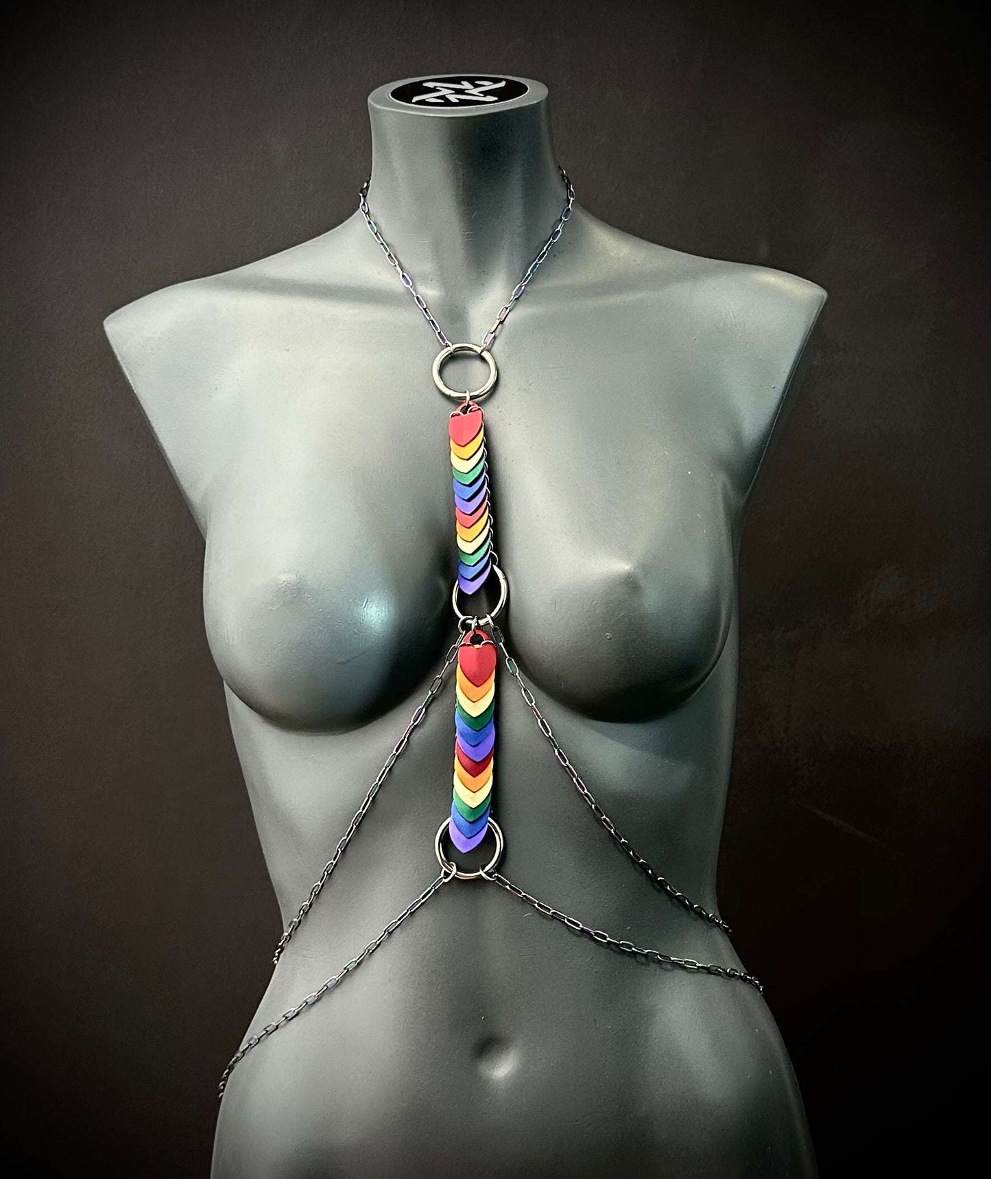 Body chain jewelry with rainbow heart charms on black mannequin, modern edgy style, bold pride statement