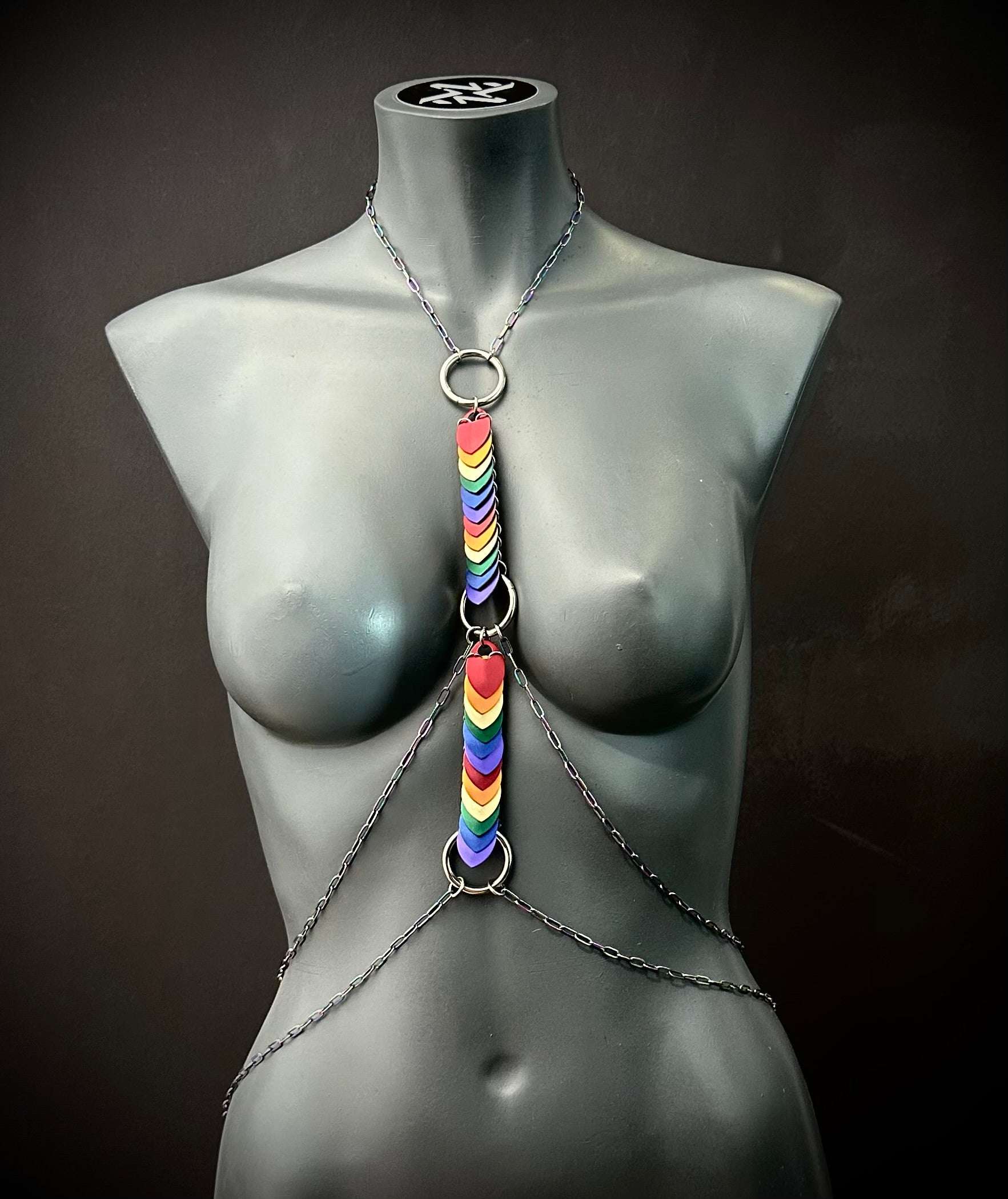 Body chain jewelry with rainbow heart charms on black mannequin, modern edgy style, bold pride statement