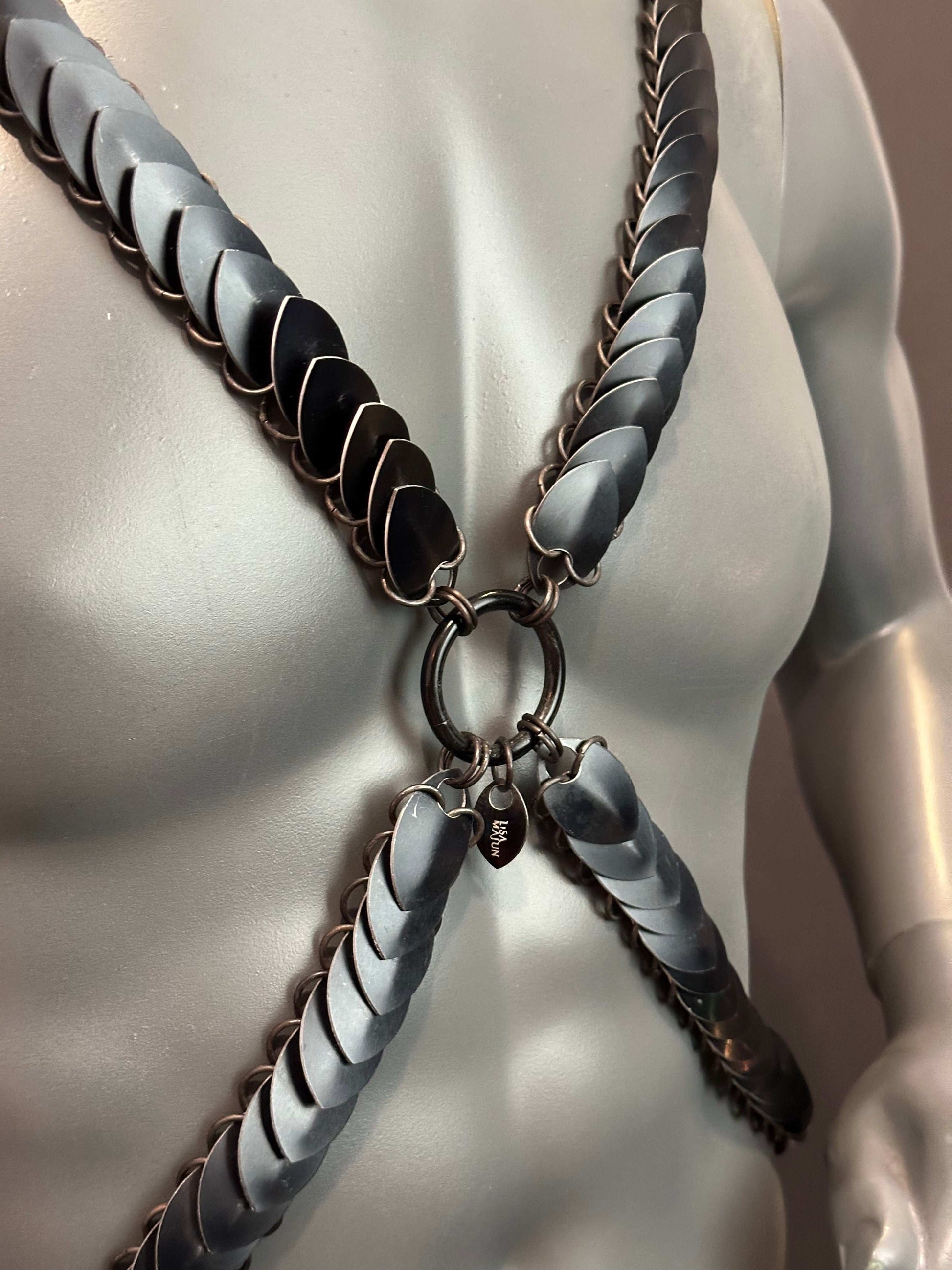 metal chest harness with matte black and grey scale-like plates on a gray mannequin, bold and edgy