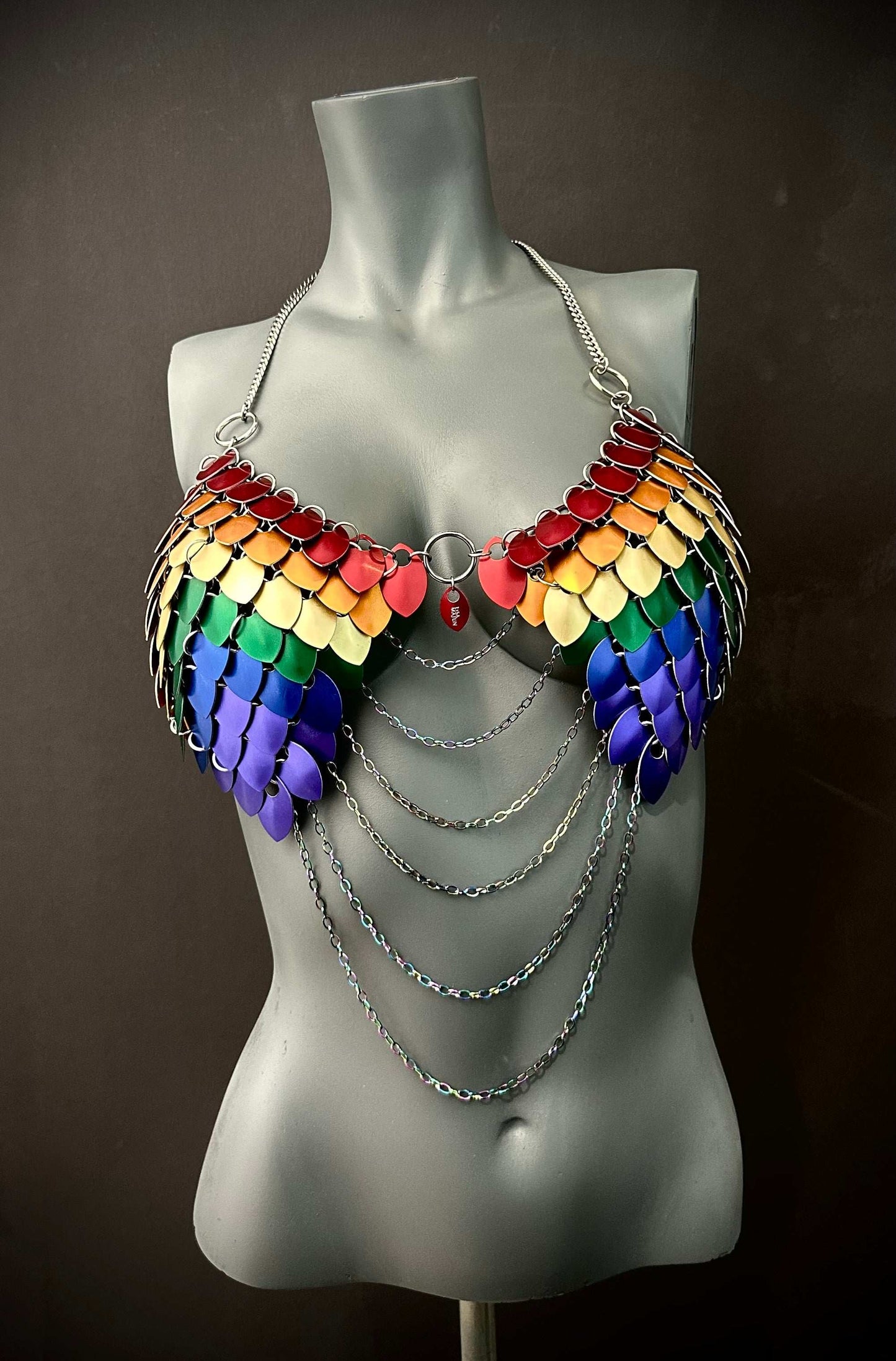 Rainbow scale metal bra with silver chains on gray mannequin, bold and vibrant style, expressive and confident