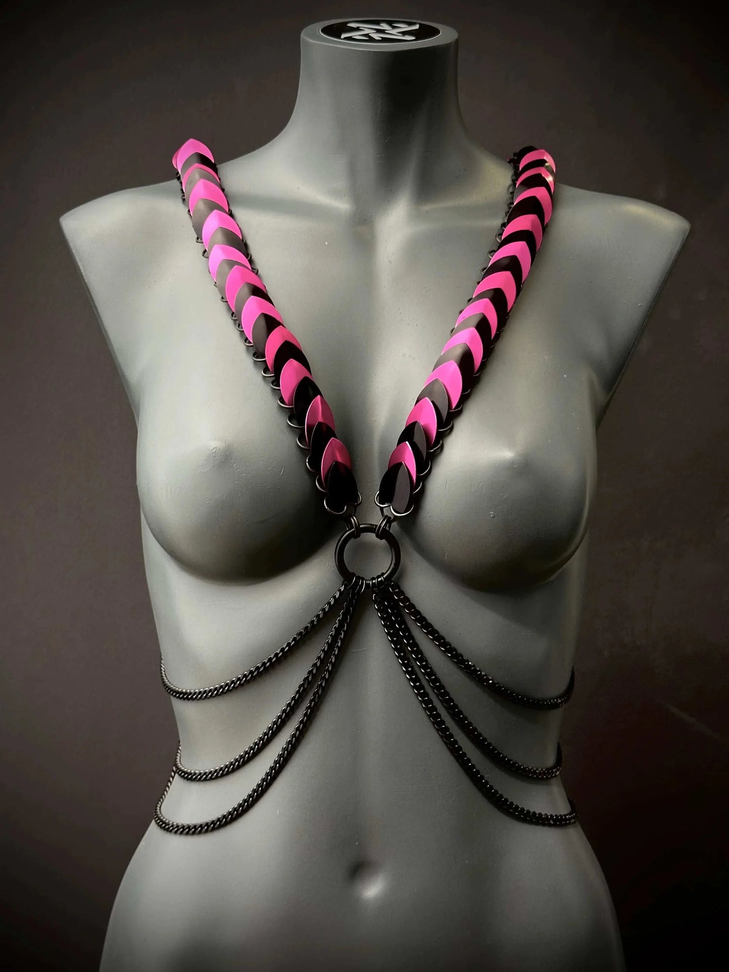 Body harness with pink and black scales and black chains on gray mannequin, edgy and bold style