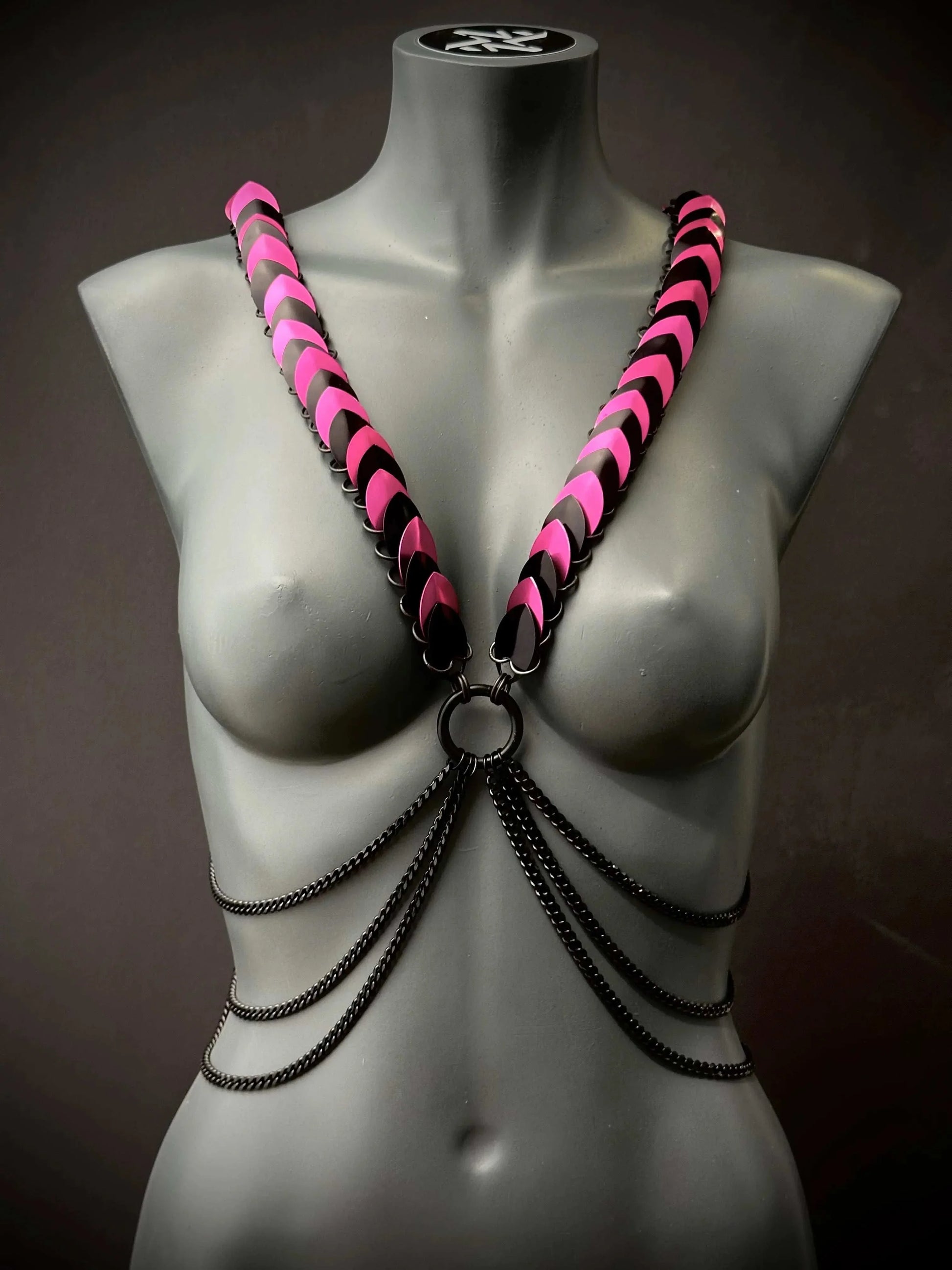 Body harness with pink and black scales and black chains on gray mannequin, edgy and bold style