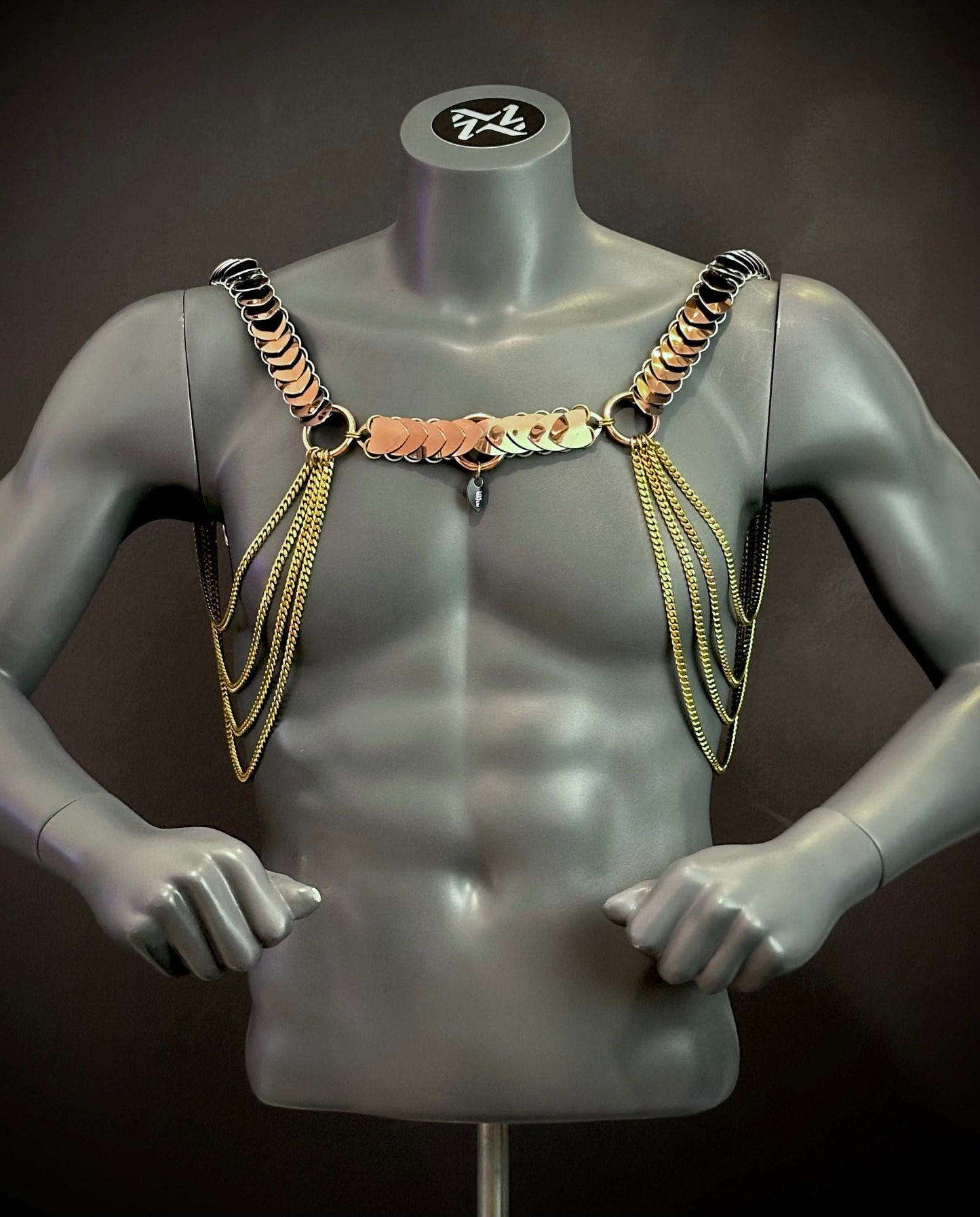 Men's gold metal chain harness with circular links on gray mannequin, bold edgy fashion style