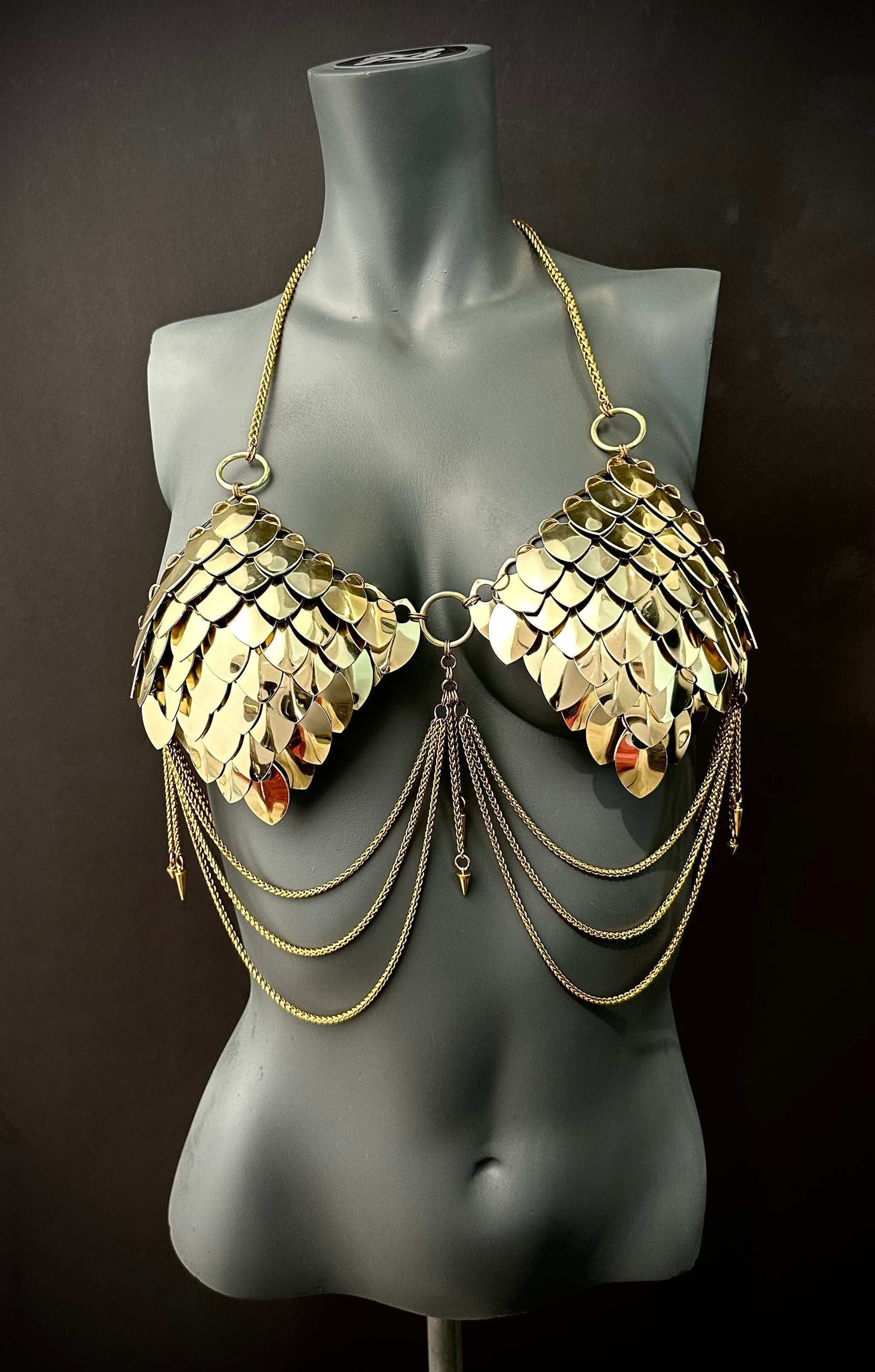 Gold metal scale bra with chains on gray mannequin, edgy style, bold confident vibes