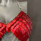 Red scale metal bra with silver chains on gray mannequin, bold and edgy fashion statement