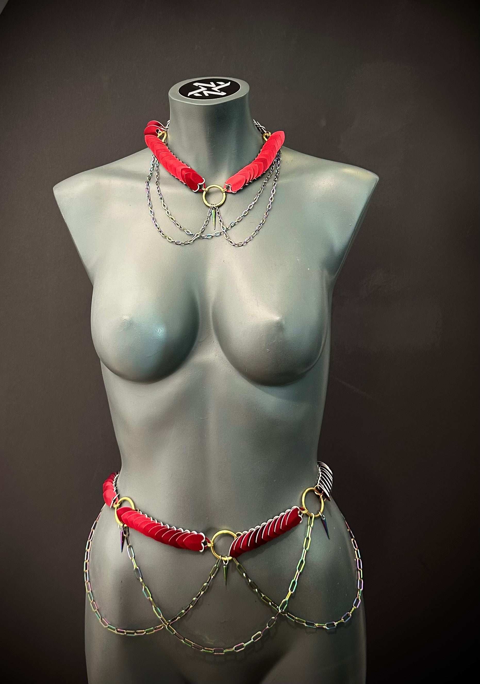 Body chain jewelry in red and gold with black spikes, edgy and bold style on matte gray mannequin
