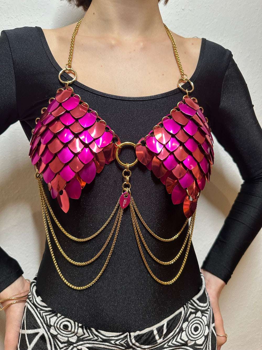 Metallic pink scale bra with gold chains styled over black top, bold and edgy feel