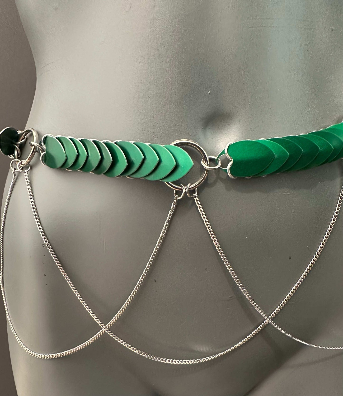 green heart-shaped scale chain belt with silver rings and draped silver chains on gray mannequin for edgy style