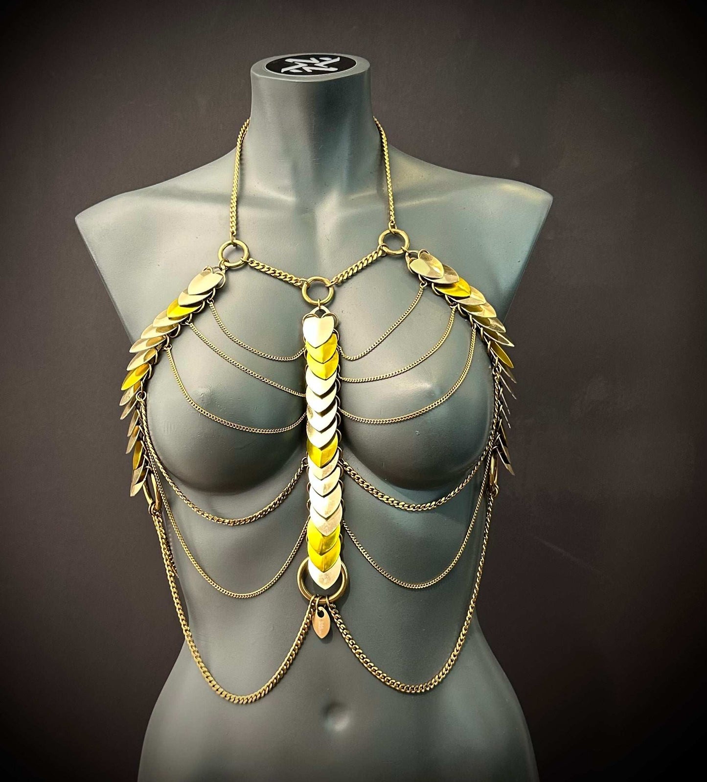 Gold body chain with heart-shaped metallic plates and elegant chains on gray mannequin, stylish and bold