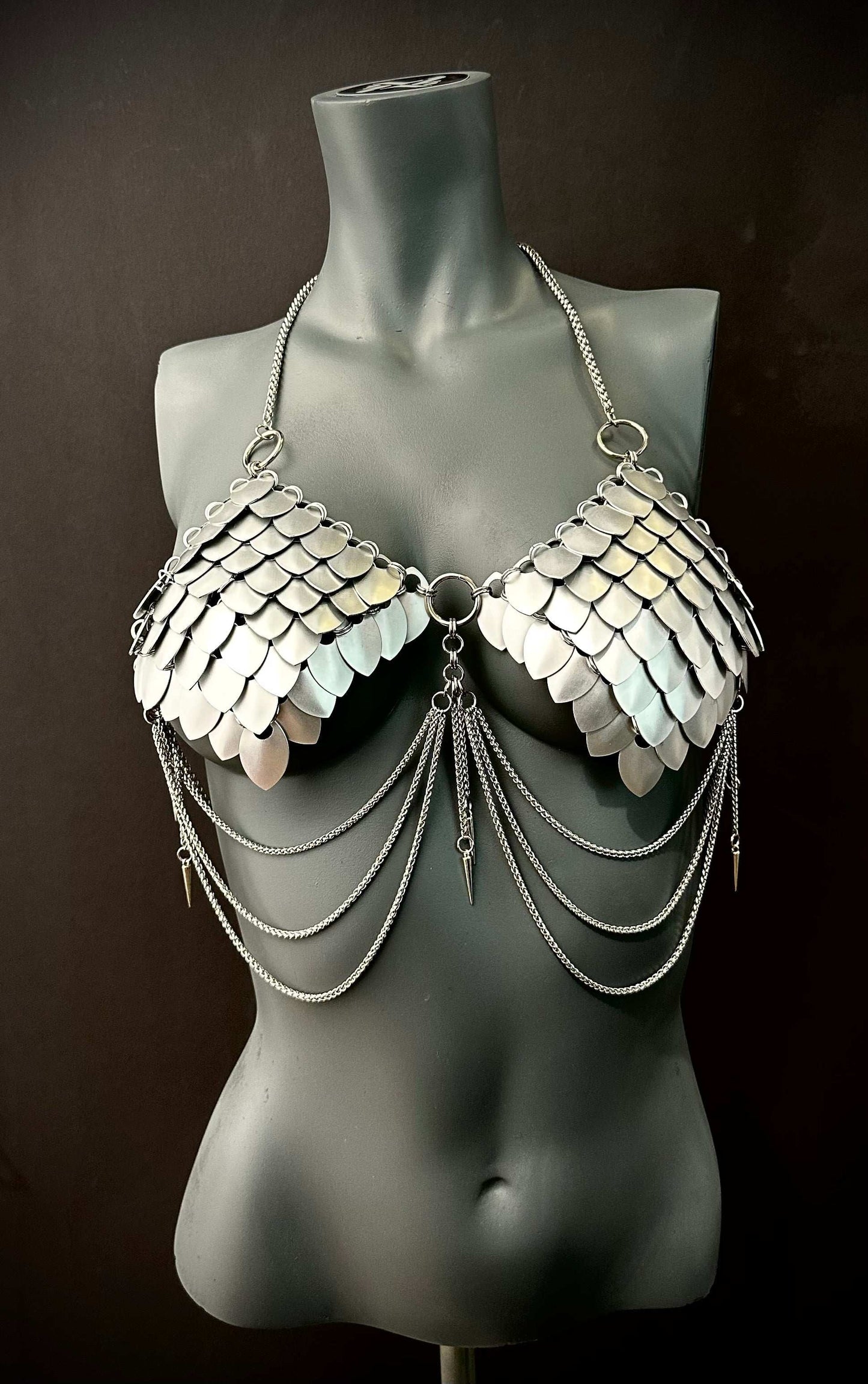Silver metal scale bra with chain drapes on gray mannequin, edgy style, bold confidence