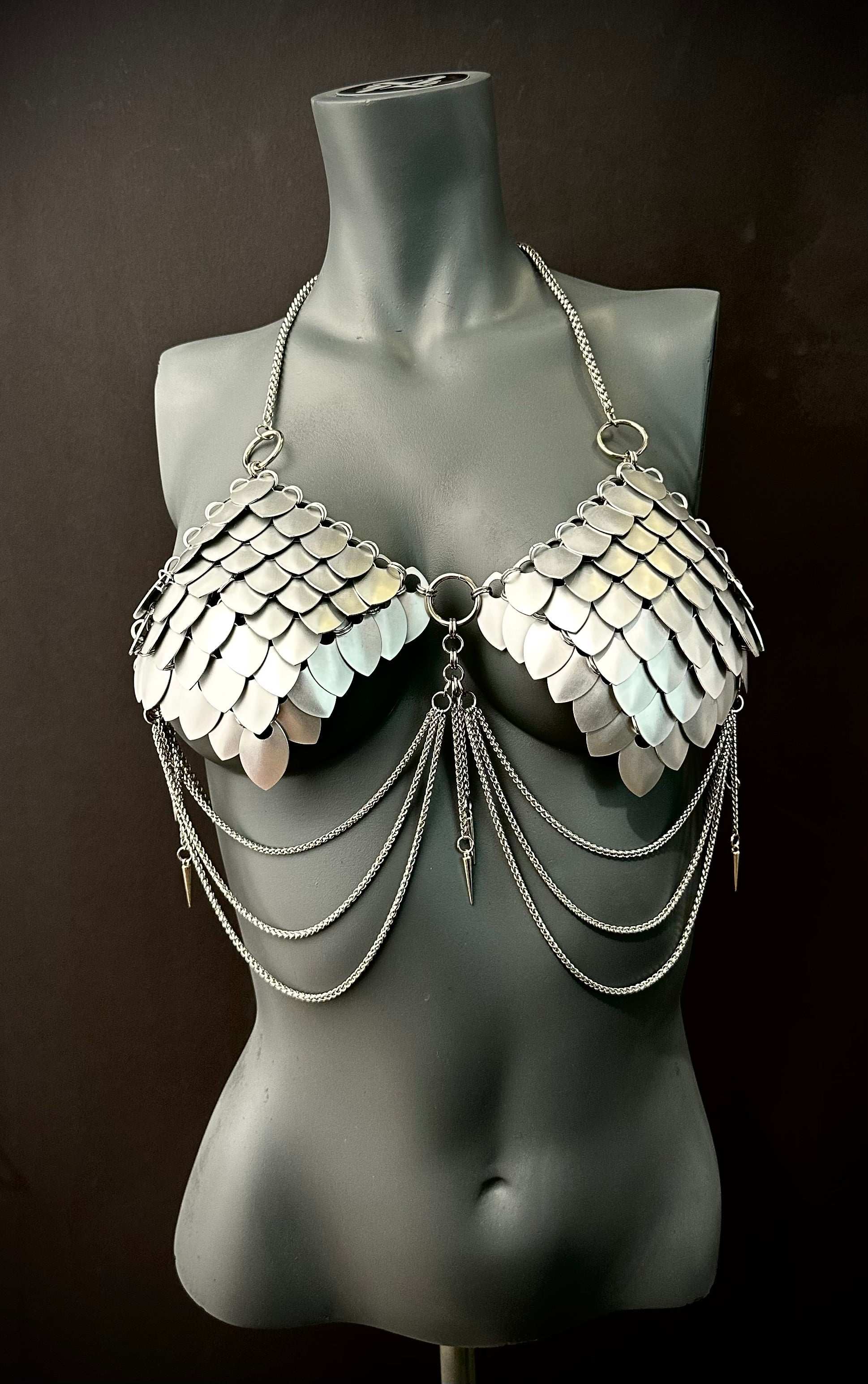Silver metal scale bra with chain drapes on gray mannequin, edgy style, bold confidence