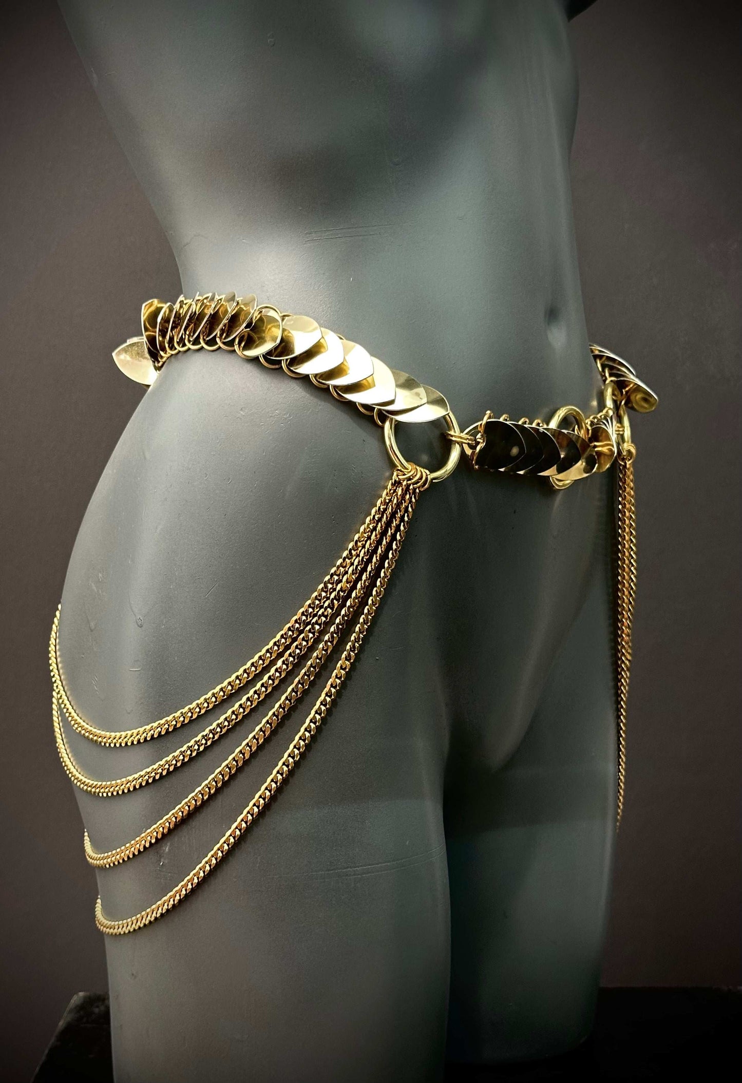 Gold metal chain belt with decorative discs and hanging chains on dark mannequin, elegant and bold