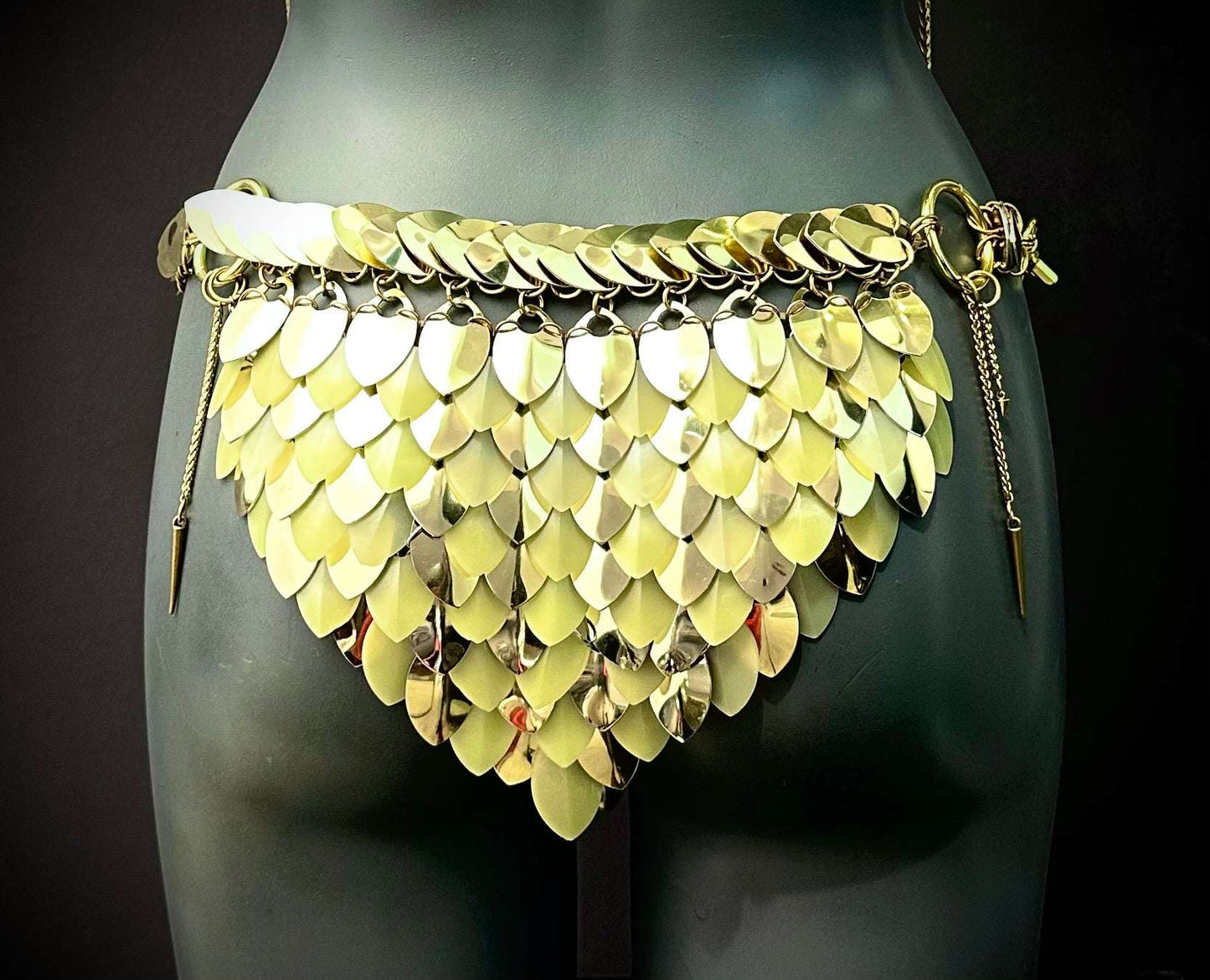 Gold metal scale belt with layered leaf-shaped plates on dark mannequin, bold and edgy fashion