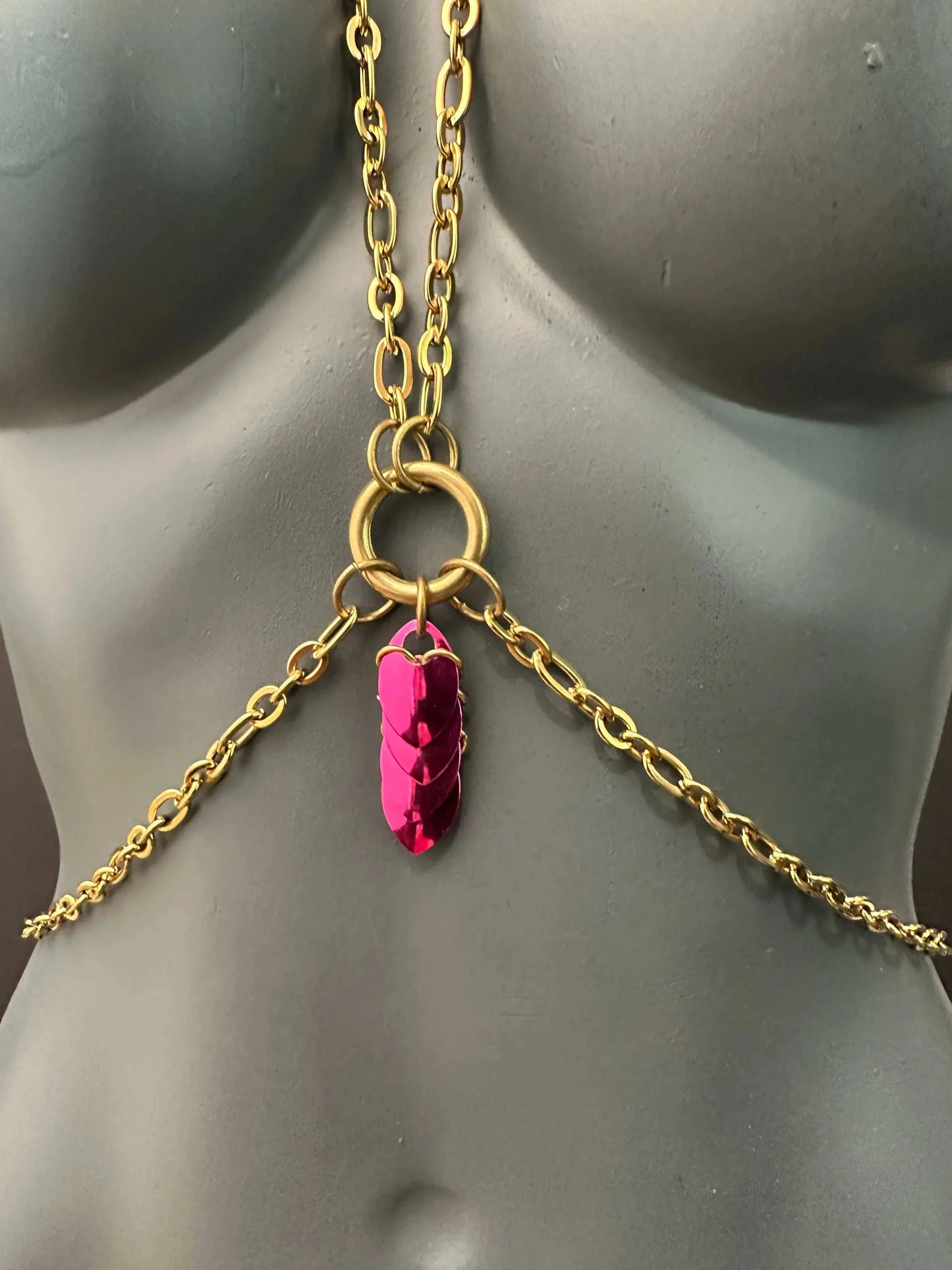 Gold body chain jewelry with a bold pink pendant on a gray mannequin, stylish and striking
