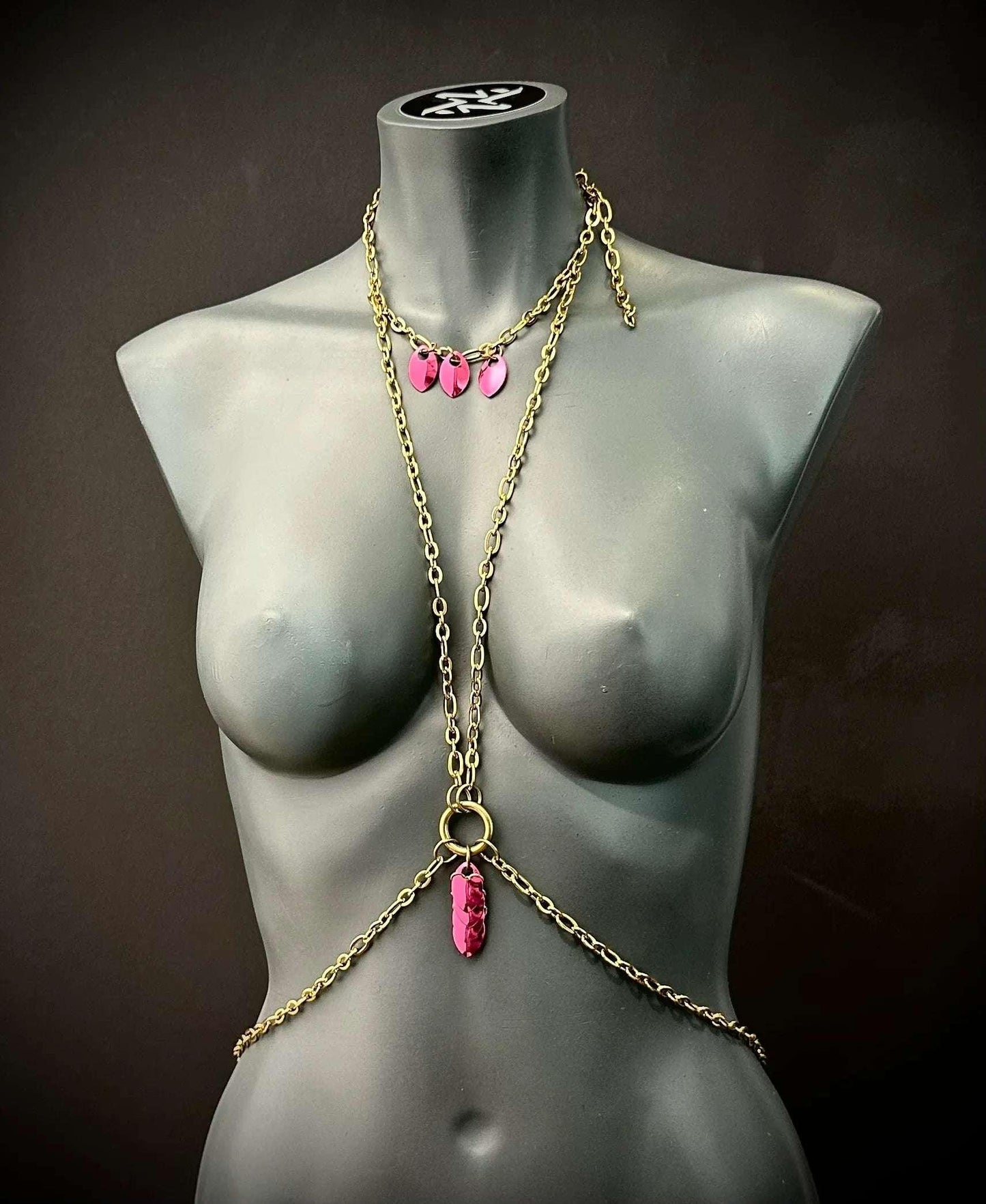Body chain jewelry in gold with pink pendants on black mannequin, elegant and bold style