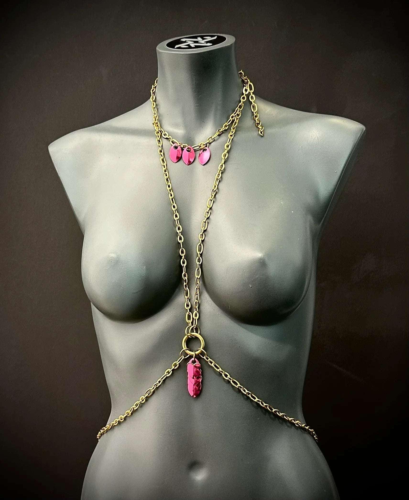 Body chain jewelry in gold with pink pendants on black mannequin, elegant and bold style