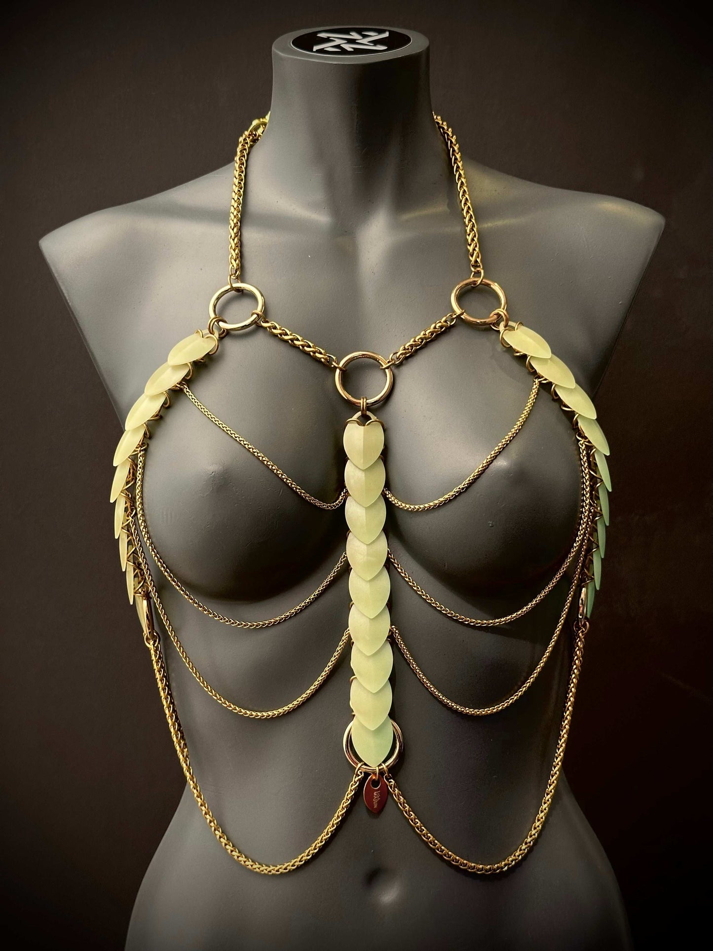 Golden body chain jewelry with green leaf accents on black mannequin, elegant and bold
