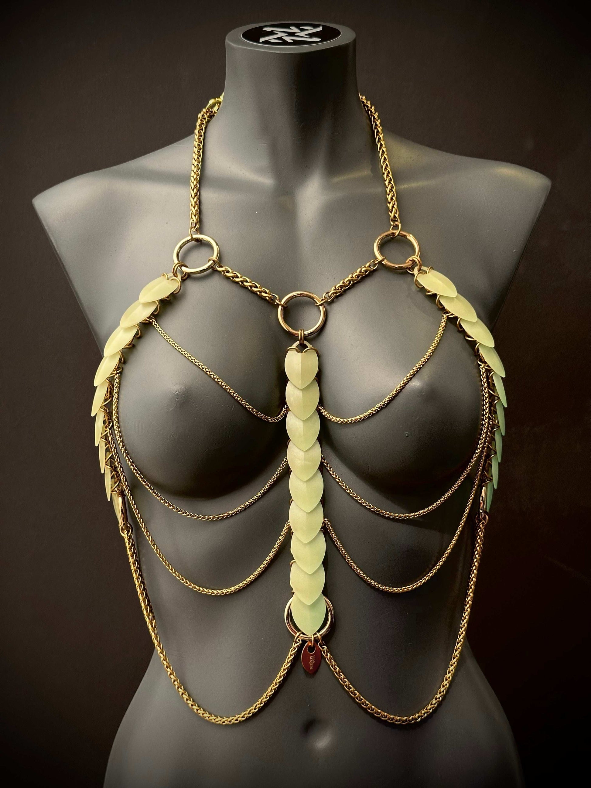 Golden body chain jewelry with green leaf accents on black mannequin, elegant and bold