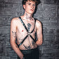 leather chest harness in black on tattooed man with curly hair and blue eyes, edgy and bold style, confident emotion